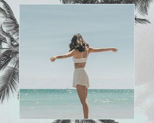 一名女子站在沙滩上，双手伸在水面前
