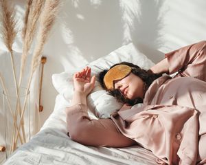 女人睡眠眼罩和温文尔雅的睡衣在床上旁边蒲苇的花瓶