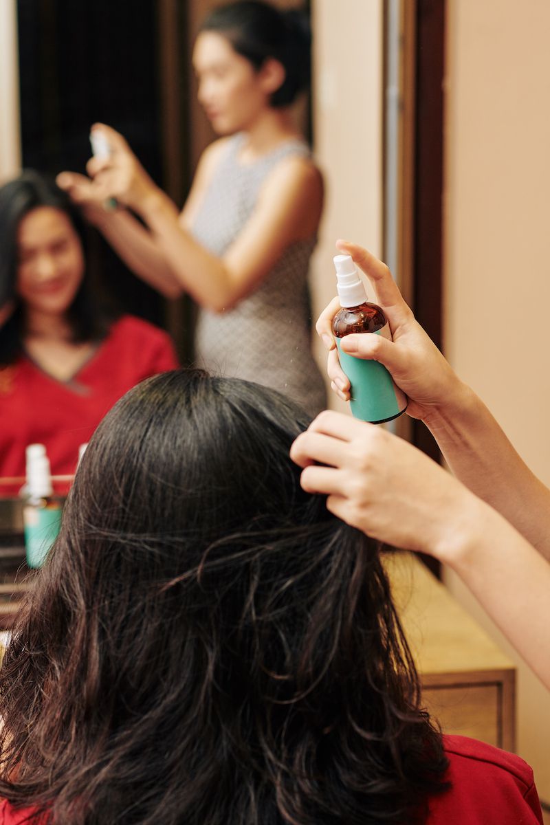 发型师在女性客户的头发上喷热保护喷雾，然后用热工具卷发