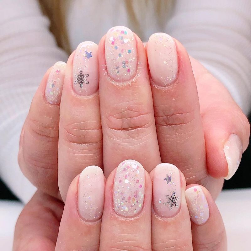 淡粉色的指甲上有银色的雪花贴花和闪闪发光的五彩纸屑
