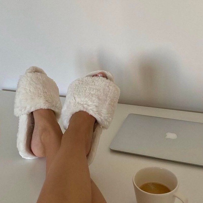 脚穿露脚的毛茸茸的白色的拖鞋,MacBook和一杯咖啡
