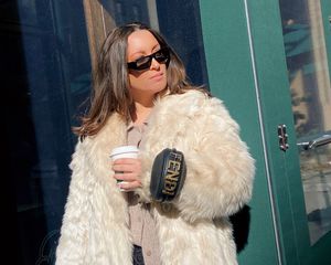 Byrdie作家贝拉杰拉德戴着黑色芬迪手镯包、太阳镜、和奶油毛皮大衣