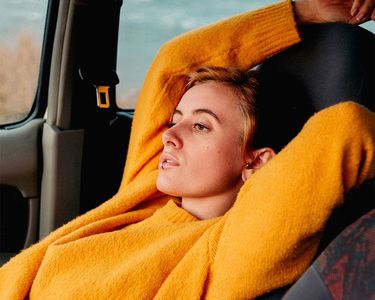 穿橙色毛衣的女人斜倚在汽车座椅上