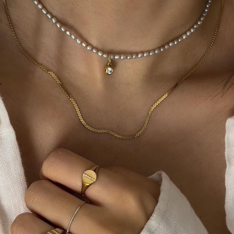 女人戴着极简主义的珍珠和金项链和戒指